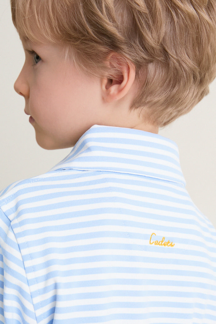 Child in a classic, light blue-and-white striped Bachelor's Blue and White Le Club Polo, featuring discreet yellow Cadets embroidery on the back, embodying effortless, high-end style.