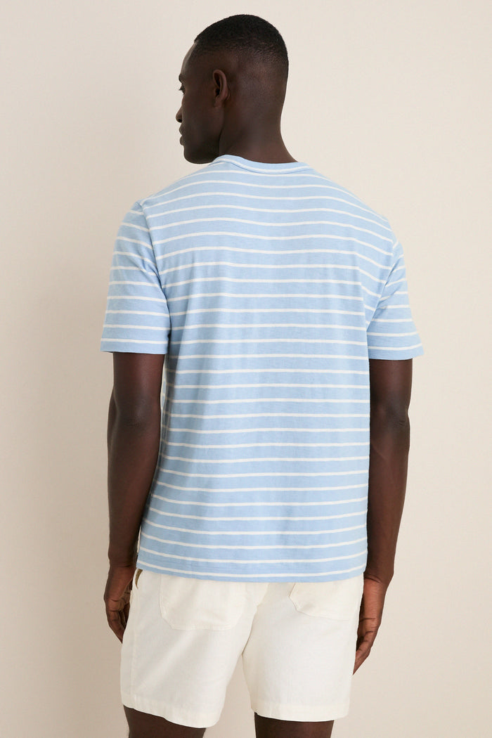 Man wearing Bermuda Sail Stripe Sunwashed Tee in light-blue with white stripes, showcasing its classic, effortless style and high-end, fun design for a relaxed, nautical look.