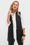 A woman wears a white button-up shirt and a Barbour x Tuckernuck black quilted vest with front pockets and a reversible Paisley liner, posing against a plain light background.