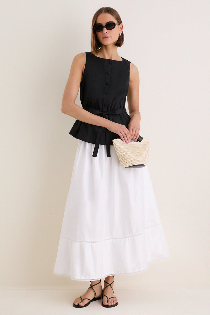Model wearing the Black Cotton Poplin Francoise Top, featuring a high neckline, sleeveless design, and cinched waist with self-tie, paired with a tiered skirt and sandals.
