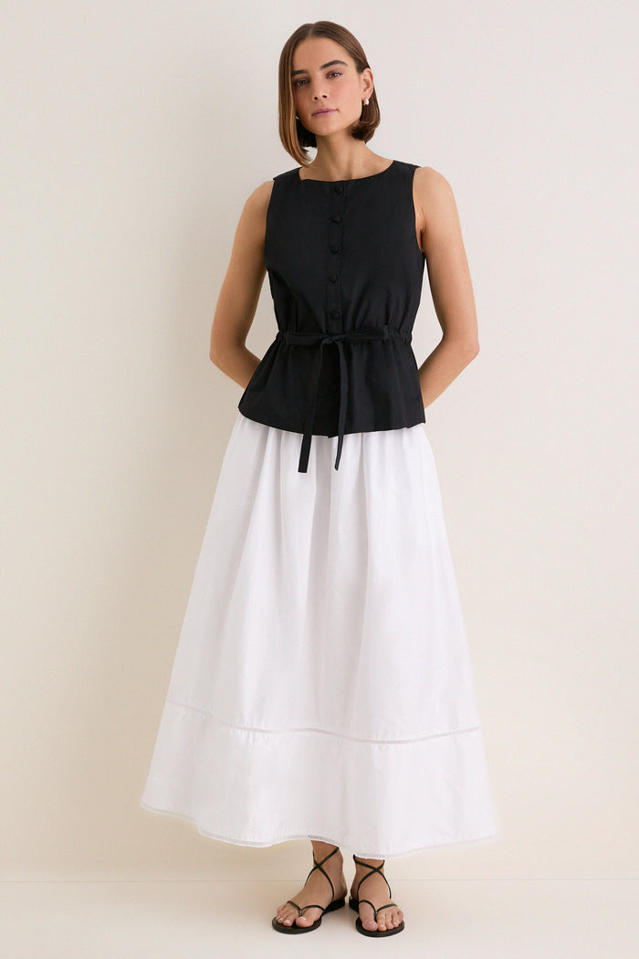 Woman models the Black Cotton Poplin Francoise Top, showcasing its classic high neckline and effortless cinched waist, paired with a flowing skirt for a high-end, fun look.