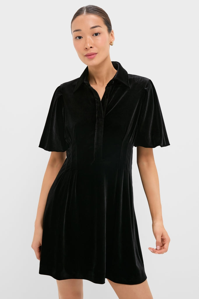 Model wears the classic Black Velvet Mini Delaney Dress with a polo collar, flutter sleeves, and A-line skirt, embodying effortless, high-end style for fun, versatile occasions.