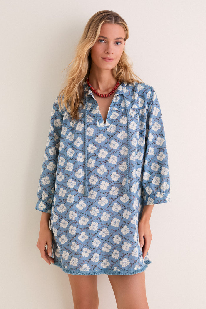 Young woman wearing the classic Bloom Lagoon Bondi Coverup, a soft blue tunic with white floral print, fringe hem, and red bead necklace, embodying effortless, high-end boho chic.