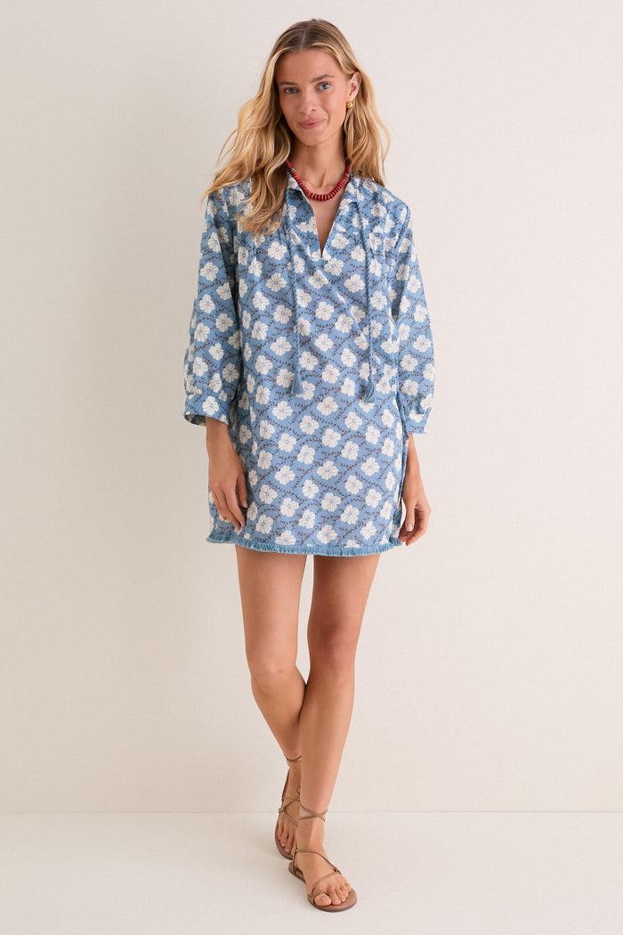 Woman models the Bloom Lagoon Bondi Coverup; an effortless, boho-chic mini dress with tassel neckties, fringed hem, and intricate embroidery, styled with sandals and accessories.
