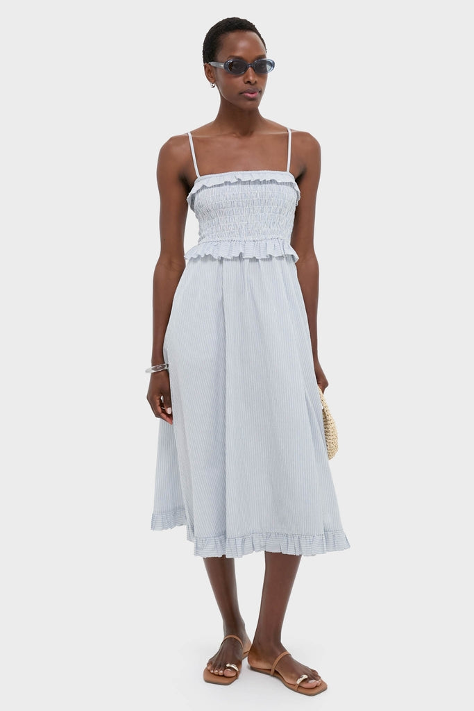 Classic Blue and White Stripe Karine Midi Dress with effortless smocked bodice, adjustable straps, and ruffle trim, styled with fun straw purse and sunglasses for a high-end look.