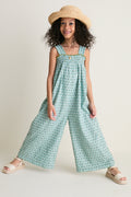 Young girl in a classic, effortless Blue Prairie Block Print Eleven Jumper, featuring a smocked bodice and wide-leg design, paired with a floppy-brim hat and espadrille sandals.