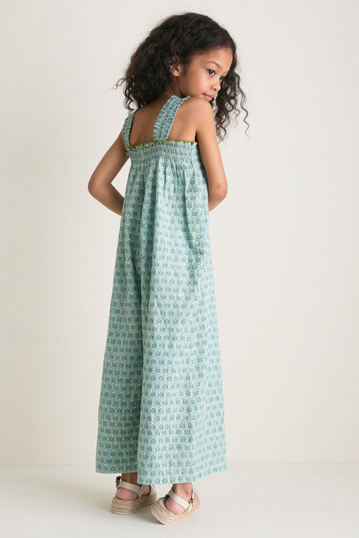 Young girl in a classic, teal-green Blue Prairie Block Print Eleven Jumper, showcasing effortless style with smocked bodice and wide-leg design, paired with beige espadrilles.