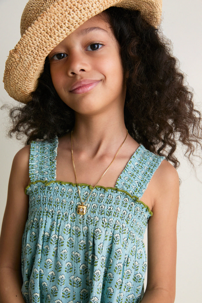 Young girl in classic Blue Prairie Block Print Eleven Jumper with smocked bodice, wide legs, and green pearl stitches, exuding effortless, high-end charm and fun.