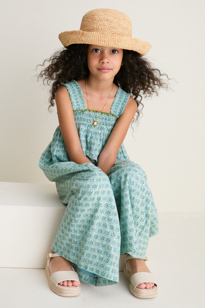 Young girl in a classic Blue Prairie Block Print Eleven Jumper with floral motifs, smocked bodice, and espadrille sandals, exuding effortless charm and high-end playfulness.