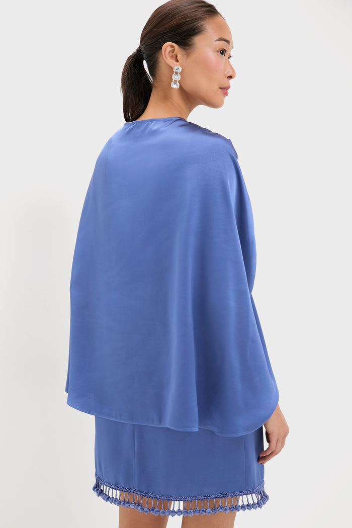 Woman in profile wearing the Blue Satin Mountbatten Cape over a matching mini skirt with fringe tassels, paired with statement earrings for an effortless, high-end, fun look.
