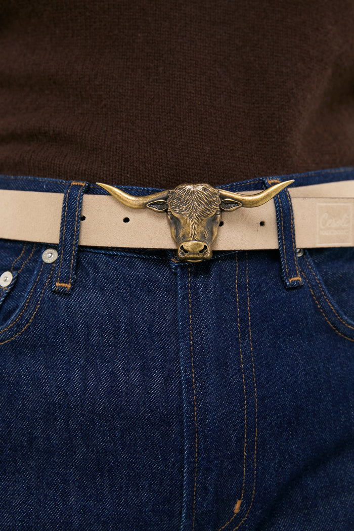 Brass Lansing Longhorn Buckle in polished brass, adorning a light-tan leather belt on dark denim jeans, offering a classic, effortless style with a high-end, fun twist.