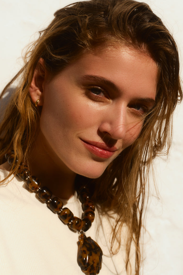 Close up of woman smiling wearing a tortoise seashell necklace.