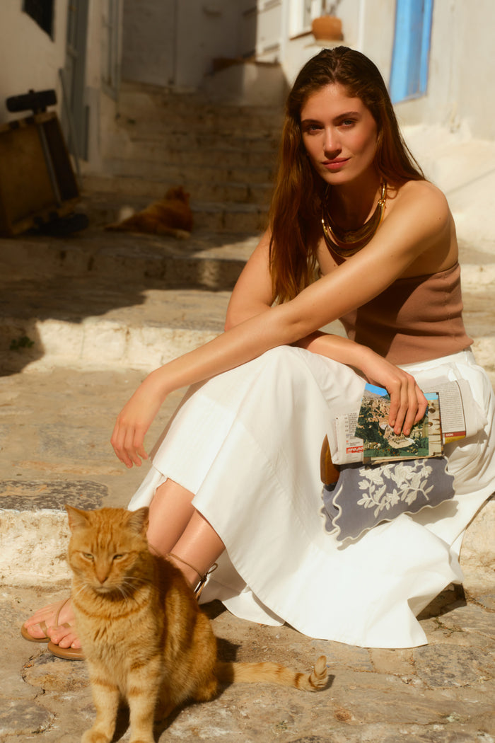 Woman sitting with a cat on stone stairs in a quiet alleyway. Woman is wearing a white skirt and a tan tube top.