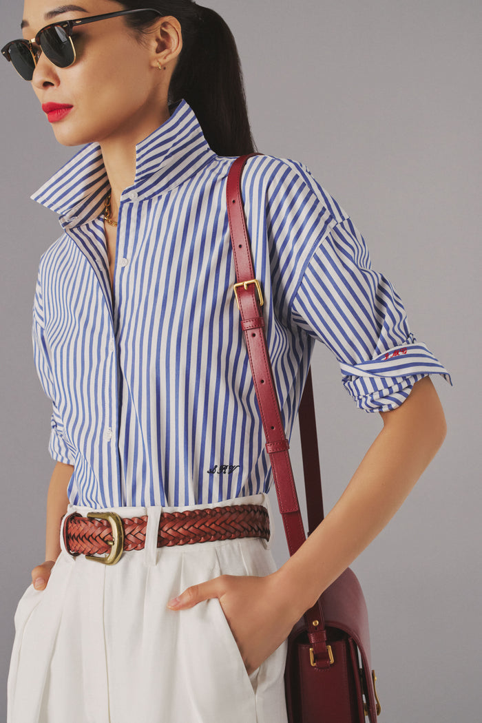 Woman in a blue and white striped button down shirt, with monogramming detail on the waist with scripted letters "SRV".