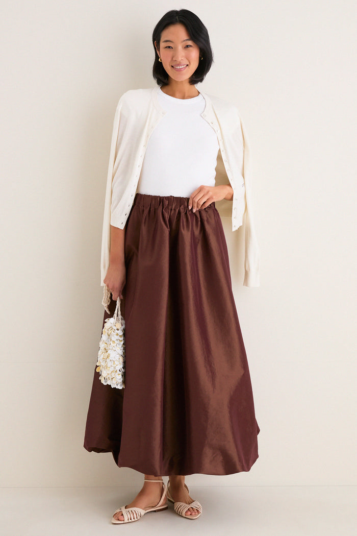 Young woman models the classic Chestnut Taffeta Cynthia Bubble Skirt, showcasing its effortless bubble hem and elastic waistband, paired with a sleeveless top and cream cardigan.
