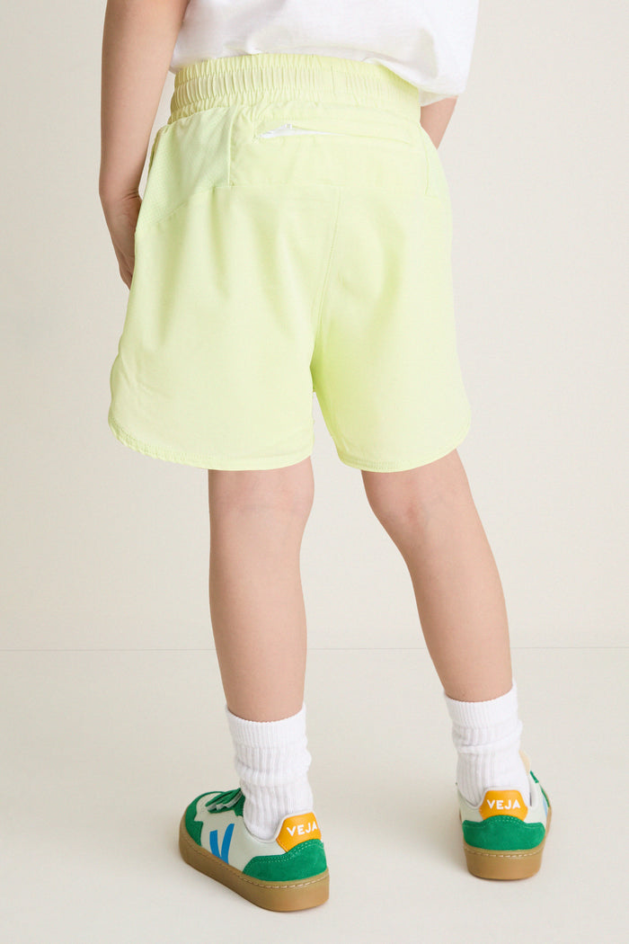 Child wearing classic Citron Zest Cardio Shorts with elastic waist, back zip pocket, and visible liner, paired with white VEJA sneakers. Effortless, fun, high-end athletic style.