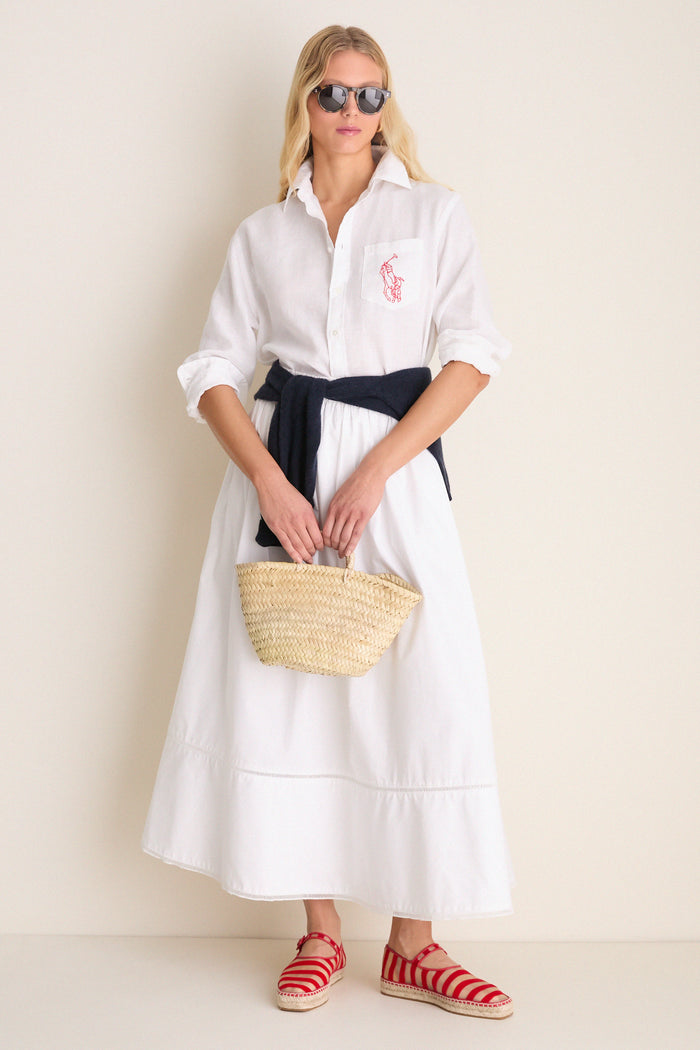 Woman in a classic Oxford white linen button-down with rolled sleeves, paired with a flowing skirt, espadrille flats, and a straw basket, exuding effortless, high-end style.