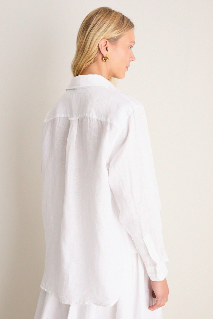Woman wearing a classic, oversized white linen button-down with gold hoop earrings, embodying effortless, high-end style. The shirt features a relaxed fit and signature details.