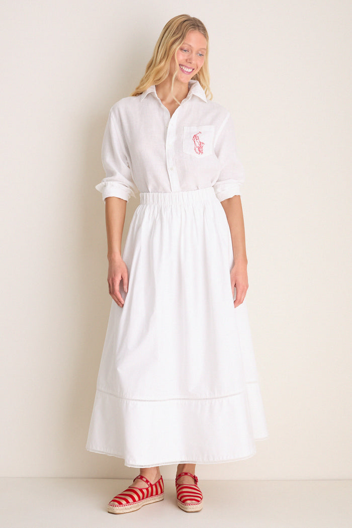 Woman in a classic Oxford white linen button-down with embroidered detail, wearing a high-waisted skirt and espadrille flats, exuding effortless, high-end style.
