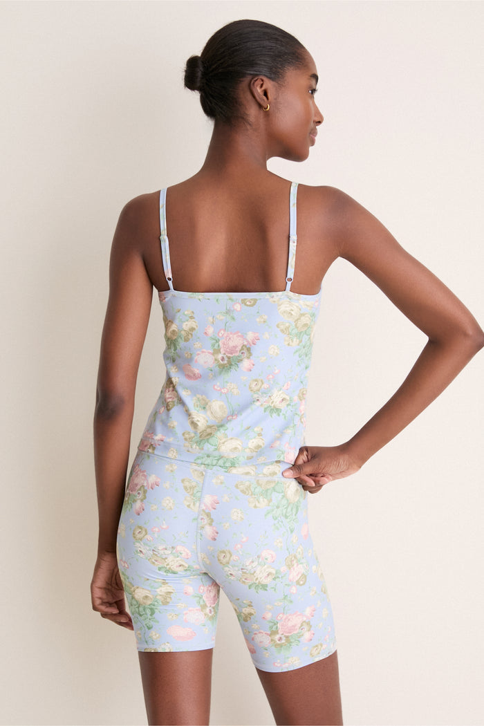 Woman in pastel-blue floral Clubhouse Chintz Compression Spandex Sofia Cami with adjustable straps, showcasing classic, effortless style. Perfect for layering or gym, offering high-end, fun fashion.