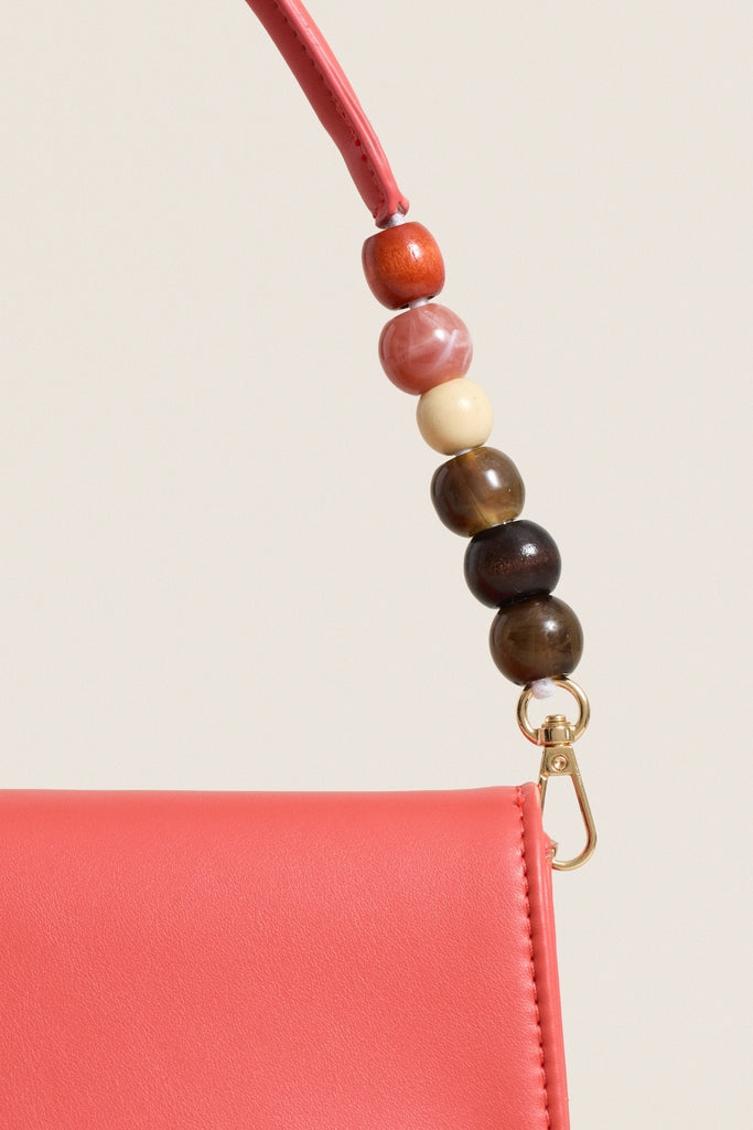 Coral Brooks Crossbody: A classic, coral clutch with an effortless flap design and fun beaded handle, featuring high-end gold-tone hardware and vegan leather.