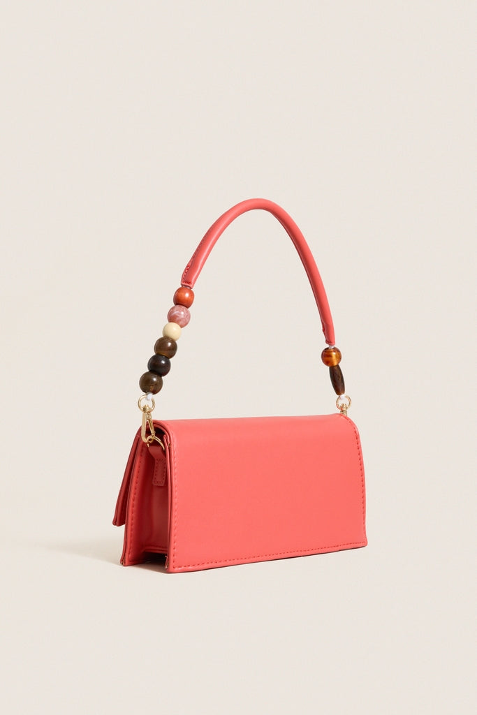 Coral Brooks Crossbody: A classic coral-pink handbag with a structured flap, multicolor beaded handle, and gold-tone hardware; effortlessly stylish for day-to-night elegance.