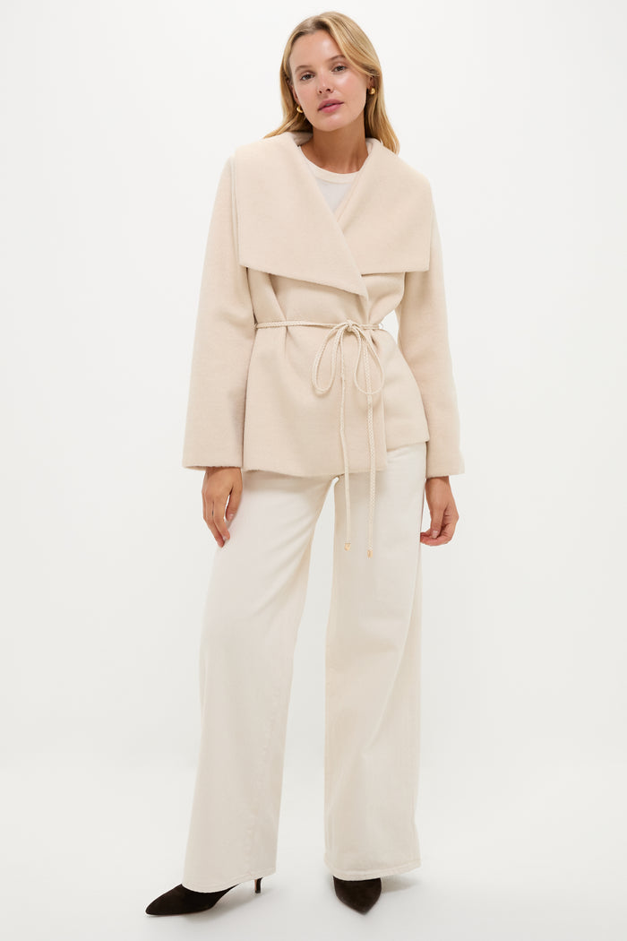 A woman stands against a white background wearing a Hyacinth House Cream Providence Wrap Jacket with an oversized collar, wide-leg cream pants, and dark pointed-toe shoes.