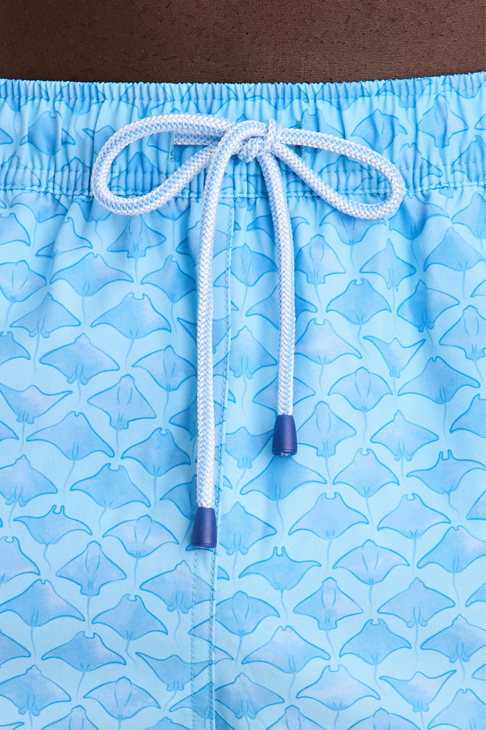 Close-up of Crystal Sea Coronado Swim Trunk showcasing light blue fabric with manta-ray pattern, elastic waist, and white drawstring, embodying Tuckernuck's effortless, high-end style.