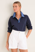 Woman models the Denim Collar Carlyn Long Sleeve Polo, a classic navy top with a denim collar, exuding effortless, high-end style, paired with white shorts.