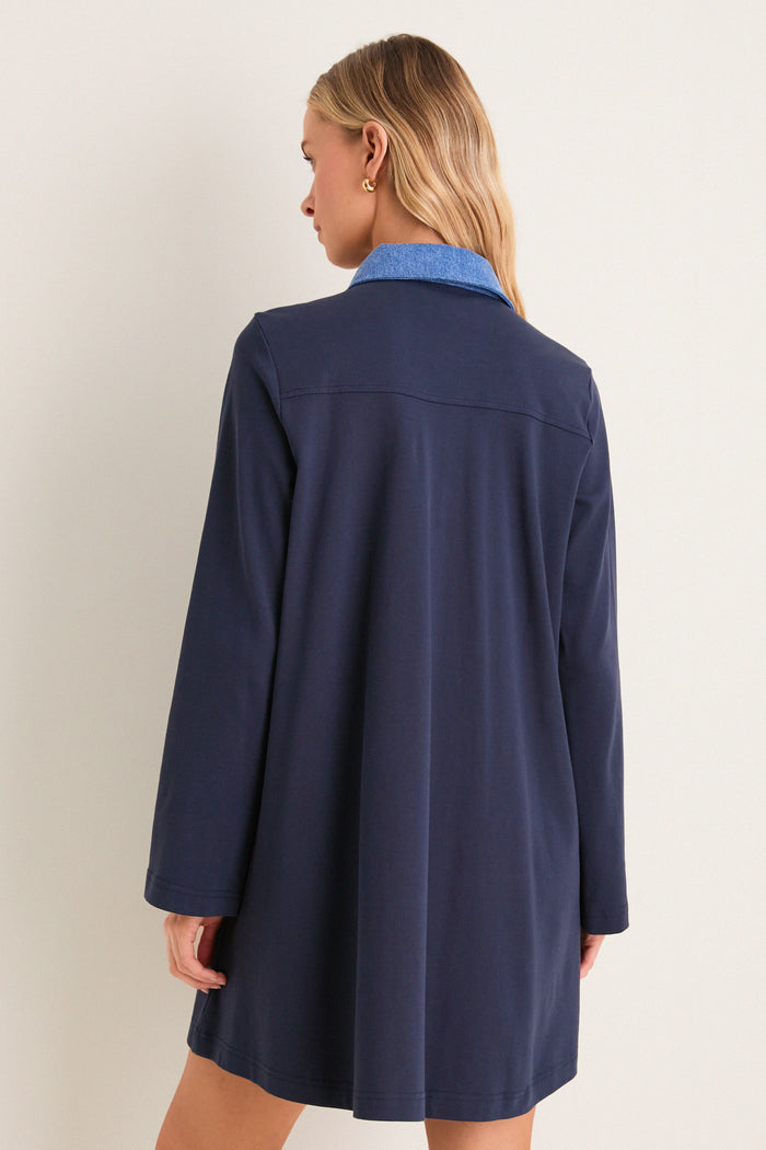 Woman wearing the Denim Collar Carolyn Swing Mini Dress, a classic, effortless tunic with a light-blue collar, embodying a fun, high-end style against a plain backdrop.