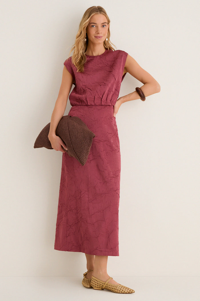 Woman models the Fig Gisella Top, a classic sleeveless, crinkled satin cropped top with relaxed silhouette, paired effortlessly with a brown clutch and gold Mary-Jane shoes.