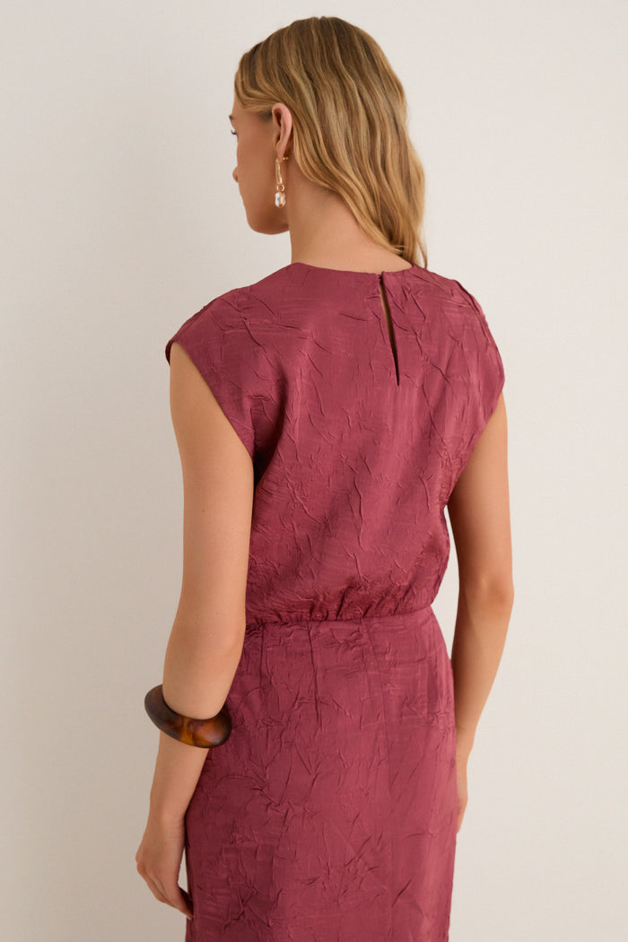 Back view of a woman in a classic, sleeveless Fig Gisella Top, showcasing its crinkled texture and elasticized waist. The look is effortlessly high-end with fun accessories.