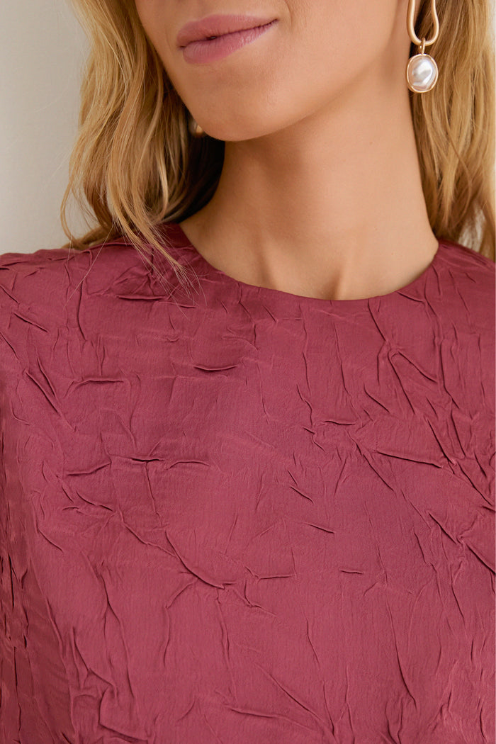 Close-up of woman wearing the Fig Gisella Top, showcasing its crinkled satin texture and elastic hem for a classic, effortless look with a high-end feel.