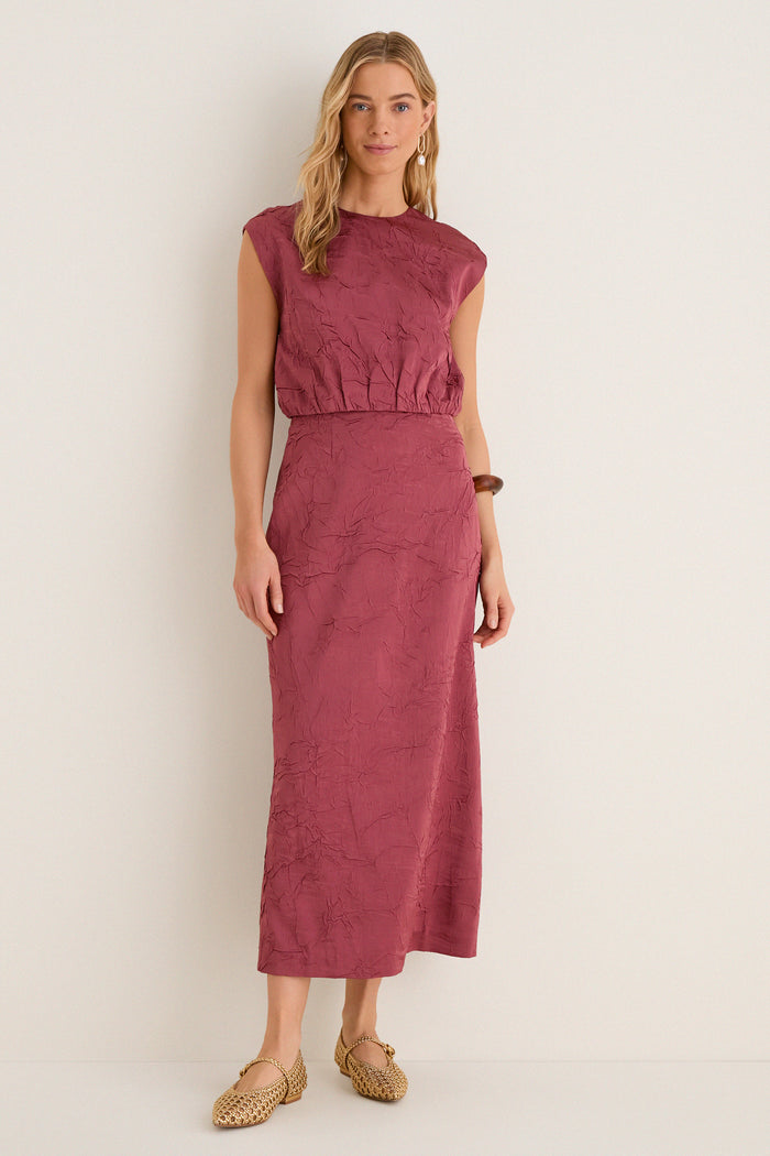 Woman in classic, sleeveless Fig Gisella Top, crinkled satin, paired with matching skirt. Effortless, high-end style: woven gold flats, wooden bangle, drop earrings.