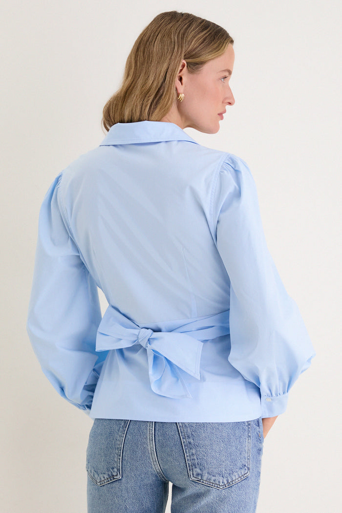 Back view of a person wearing the French Blue Tie Front Bow Bea Blouse, featuring a classic wrap design with a chic bow and slightly puffed sleeves.