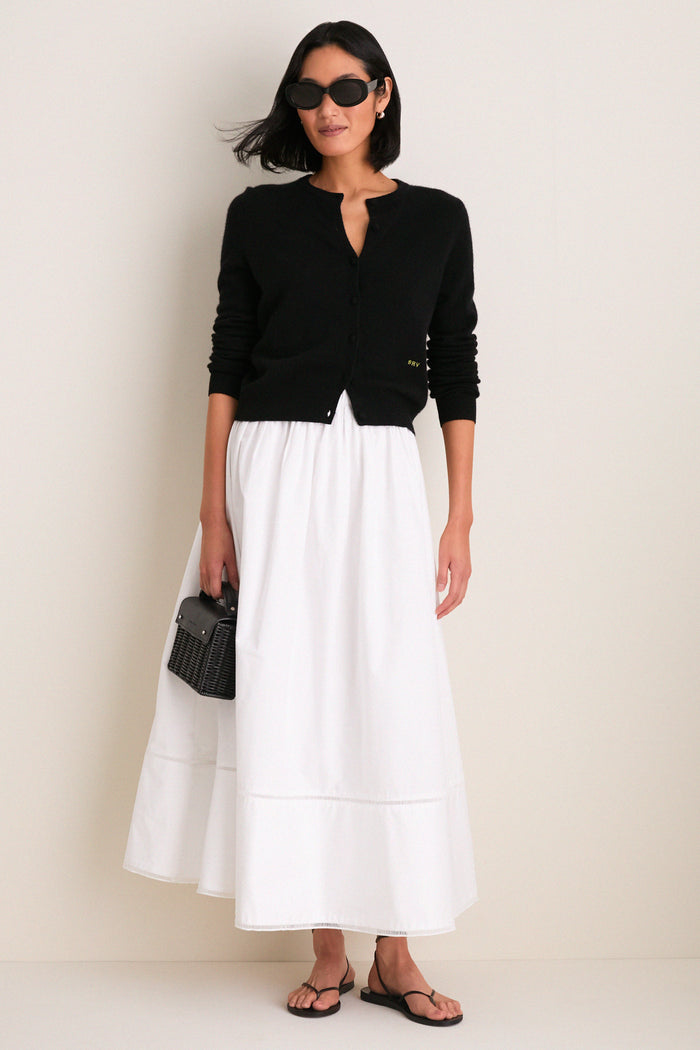 Model wearing Gloss Black Lyna Sunglasses, paired with a classic black cardigan and white skirt, exuding an effortless, high-end style with fun, bold eyewear.
