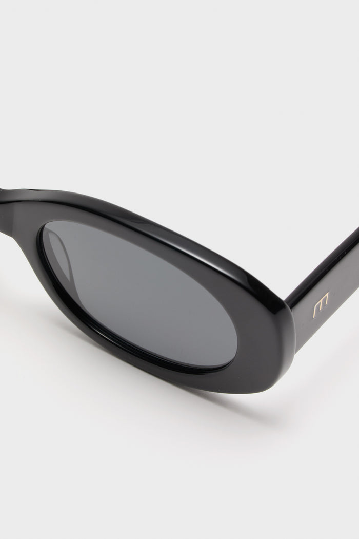 Gloss Black Lyna Sunglasses with oval acetate frame and dark tinted lenses, featuring a chic gold M logo on the temple, exude effortless, high-end style.