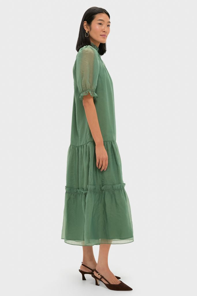 Model in profile wearing an effortless, classic Green Chiffon Selena Maxi Dress with puff sleeves and ruffled details, paired with brown suede slingback pumps.
