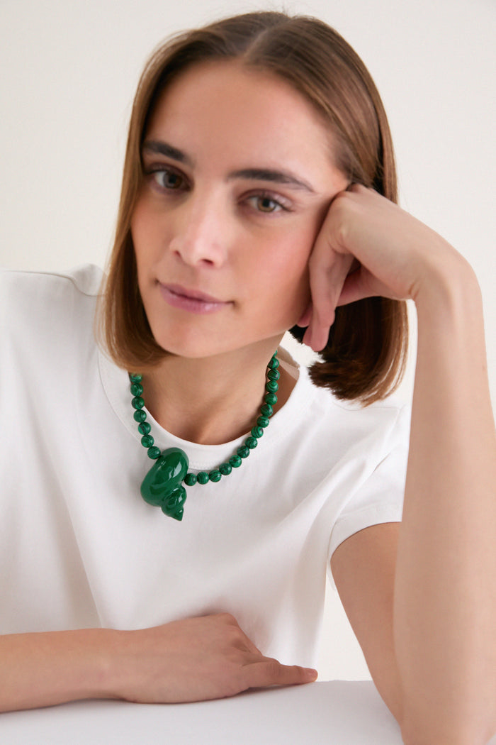Young person wearing Green Mykonos Necklace, featuring chunky malachite beads and a sculptural shell pendant, exuding a classic, effortless, and high-end style against a light background.
