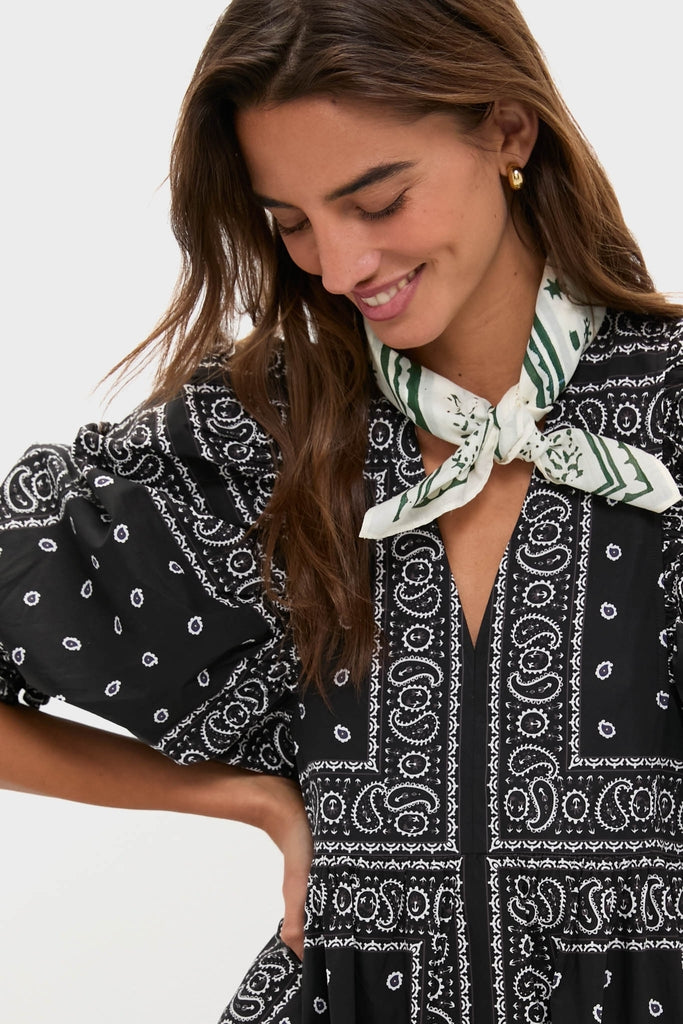Woman in black paisley-print dress wears the HB x Tuckernuck Stars at Night Scarf, a classic, effortless accessory with green star motifs. She exudes a fun, high-end vibe.