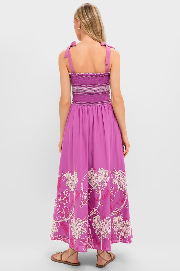 Woman in Hibiscus Embroidered Scarlett Sundress showcasing a classic, effortless style with a smocked bodice, bow tie straps, and embroidered flowing skirt, styled with brown sandals.