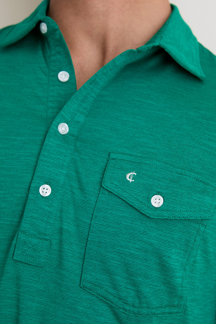 Close-up of a classic, high-end green polo shirt, featuring a 4-button placket, chest pocket with embroidery, and subtle ribbed texture, embodying effortless style and fun.