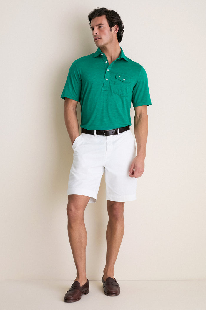 Man wearing the Home Turf Performance Sport Players Shirt, a classic, high-end bright green polo with a 4-button placket and pocket, paired with white shorts. Effortless and fun style.