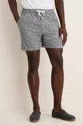 Man wearing India Ink Saturday Beach Short, featuring classic blue-and-white micro-check pattern, elastic waistband, and hidden zipper pocket, paired with a tucked-in T-shirt and suede loafers.