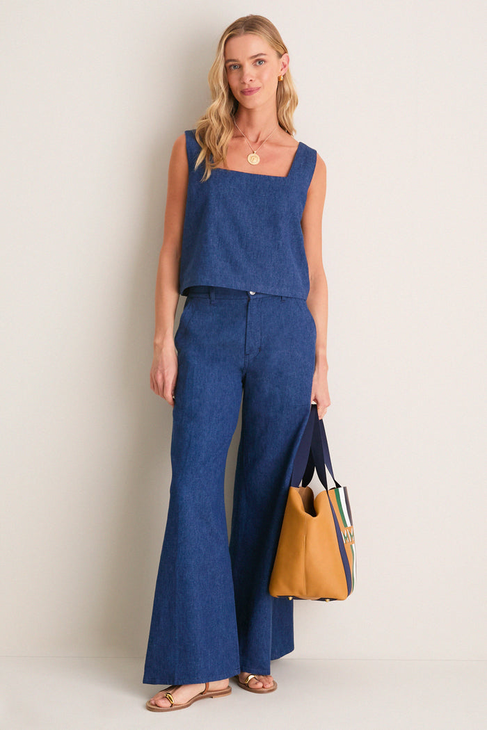 Model in classic Indigo Roma Top 2, a sleeveless, square-neck denim crop, exuding effortless style, paired with wide-leg jeans and a chic mustard stripe tote.