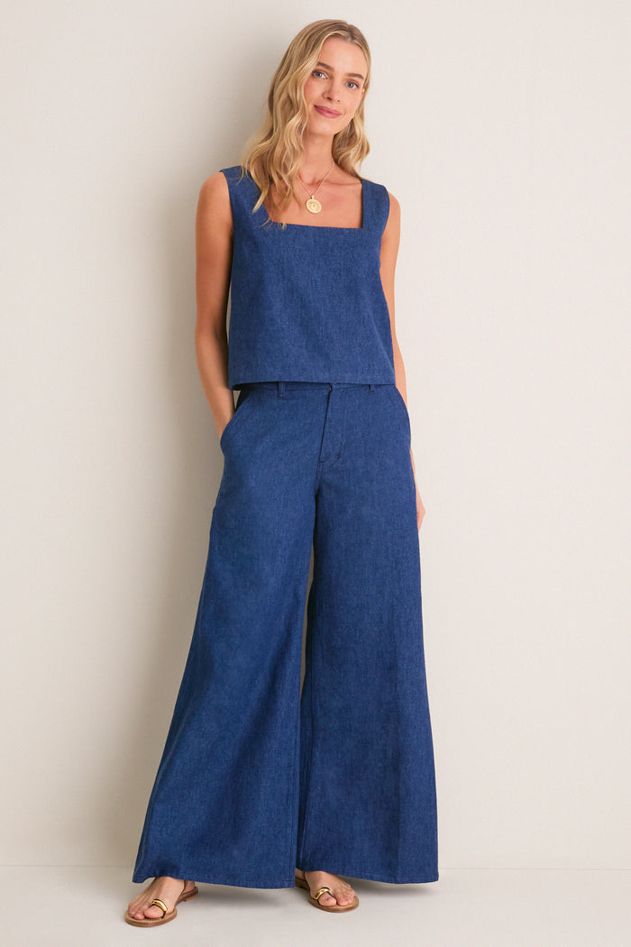 Woman models Indigo Roma Top 2, a chic, sleeveless denim tank with a square neckline and boxy fit, embodying classic, effortless style for versatile, high-end fashion.