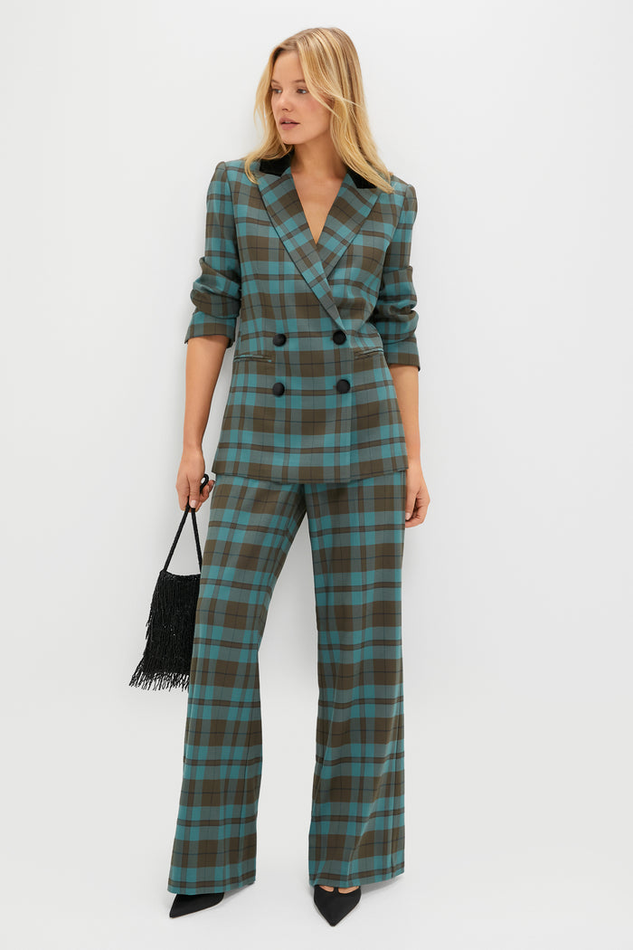 A woman stands confidently against a white background wearing a Tuckernuck teal and brown plaid blazer with wide-leg pants, paired with black pointed-toe shoes and a black fringe handbag.