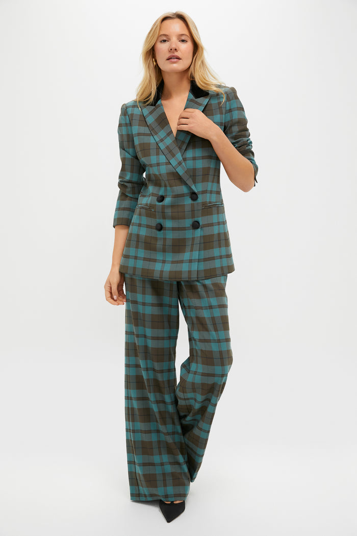 A woman wears a Tuckernuck double-breasted blue and brown plaid suit with high-rise, wide-leg trousers and black pointed shoes, standing against a plain white background.