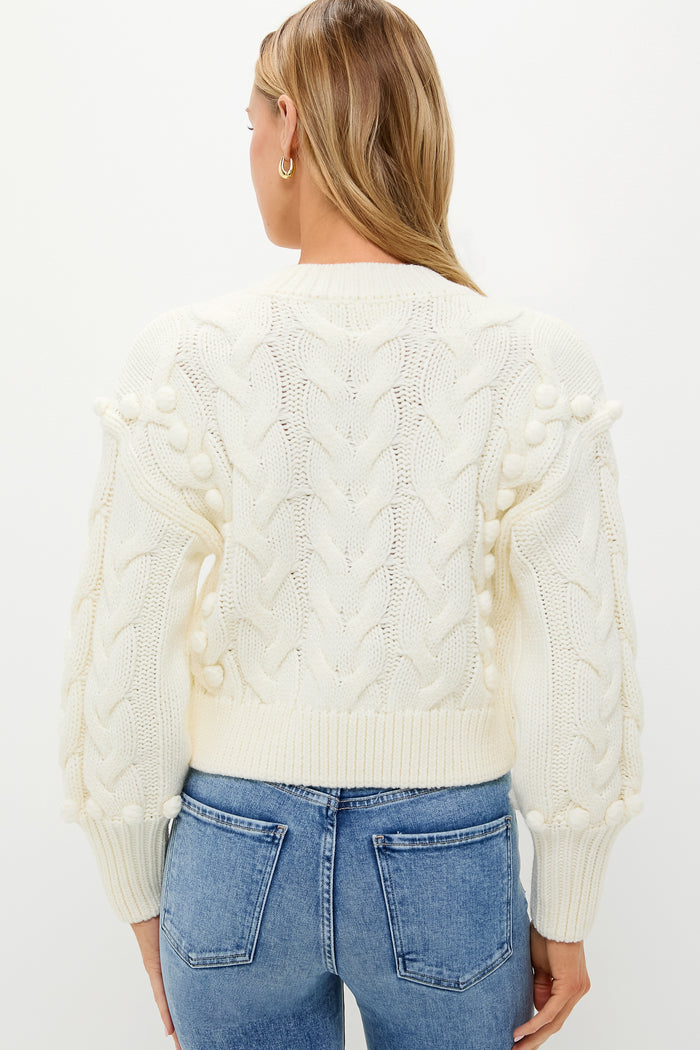 Back view of a person in the Ivory Cable Knit Cropped Contessa V-Neck Sweater, showcasing classic bobble detailing and effortless style paired with jeans.