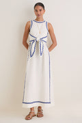 Woman models the classic White Ric Rac Tie-Front Brocks Dress, featuring effortless blue piping detail, complemented by fun gold jewelry and high-end white sandals.